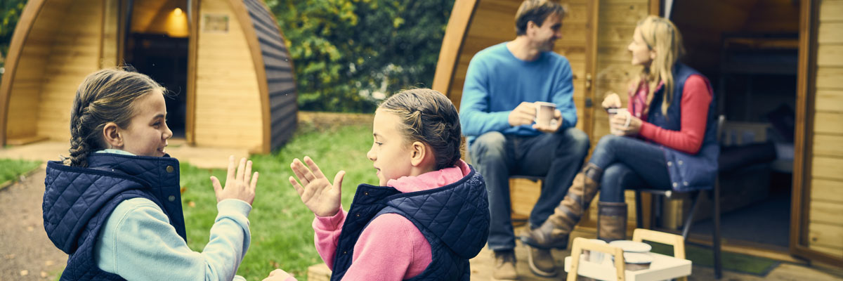 Two little girls playing with their parents in the background sitting outside a glamping pod